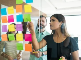 female-young-manager-discussing-adhesive-note-with-coworkers-office-meeting